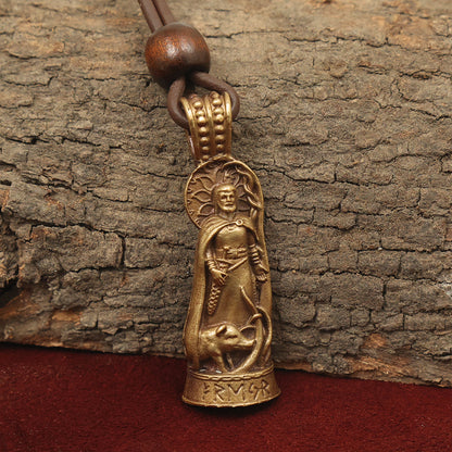 The Freyr Pendant – Lord of Abundance is a bronze Norse jewelry piece on leather cord, featuring a robed figure with halo above a coiled serpent or dragon. It rests on tree bark and red fabric; runic inscriptions in solid brass decorate the base.