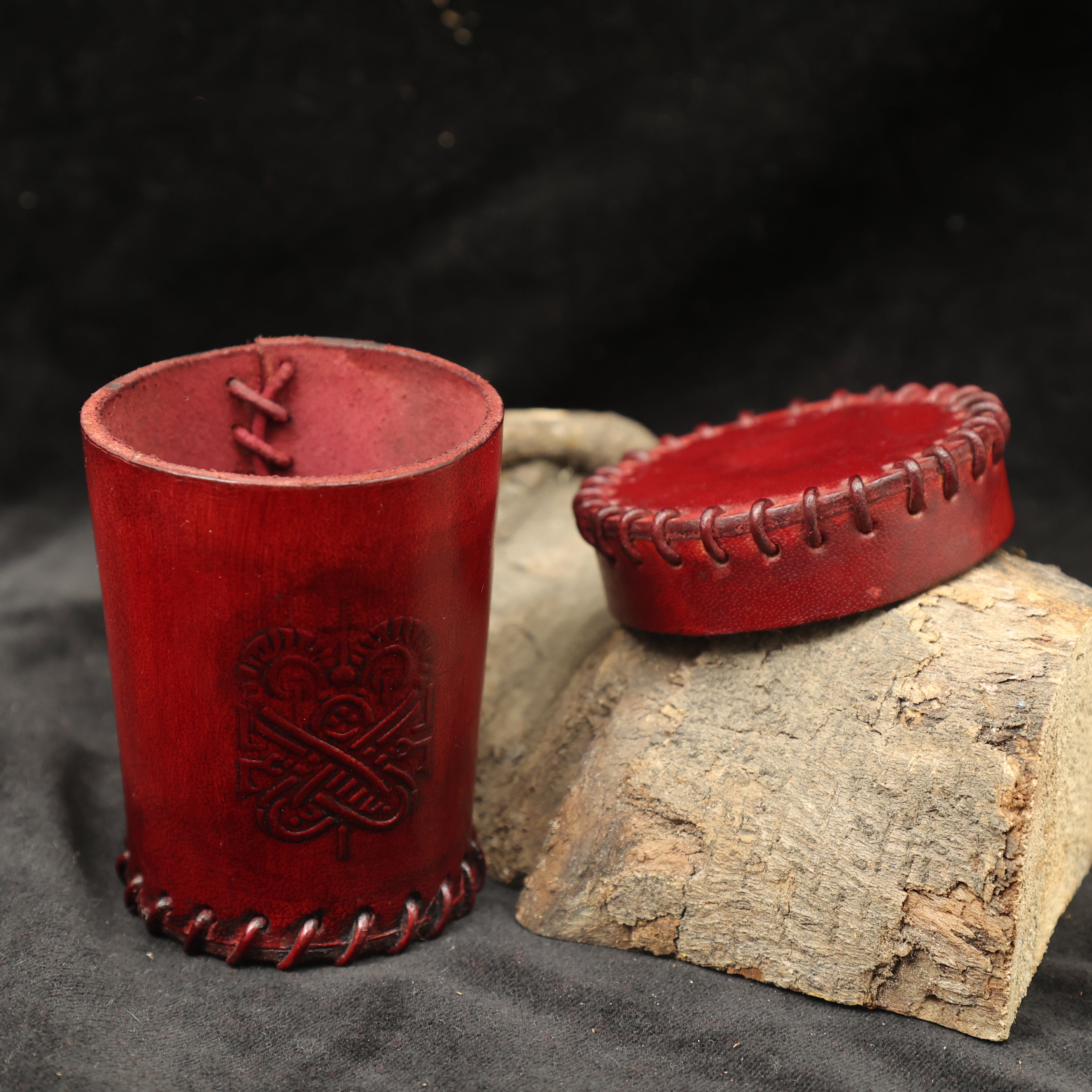 The Handcrafted Dark Red Leather Dice Cup features a stitched seam and embossed design, standing upright with its lid on rustic wood—ideal as a handmade leather dice cup for tabletop RPG accessories.
