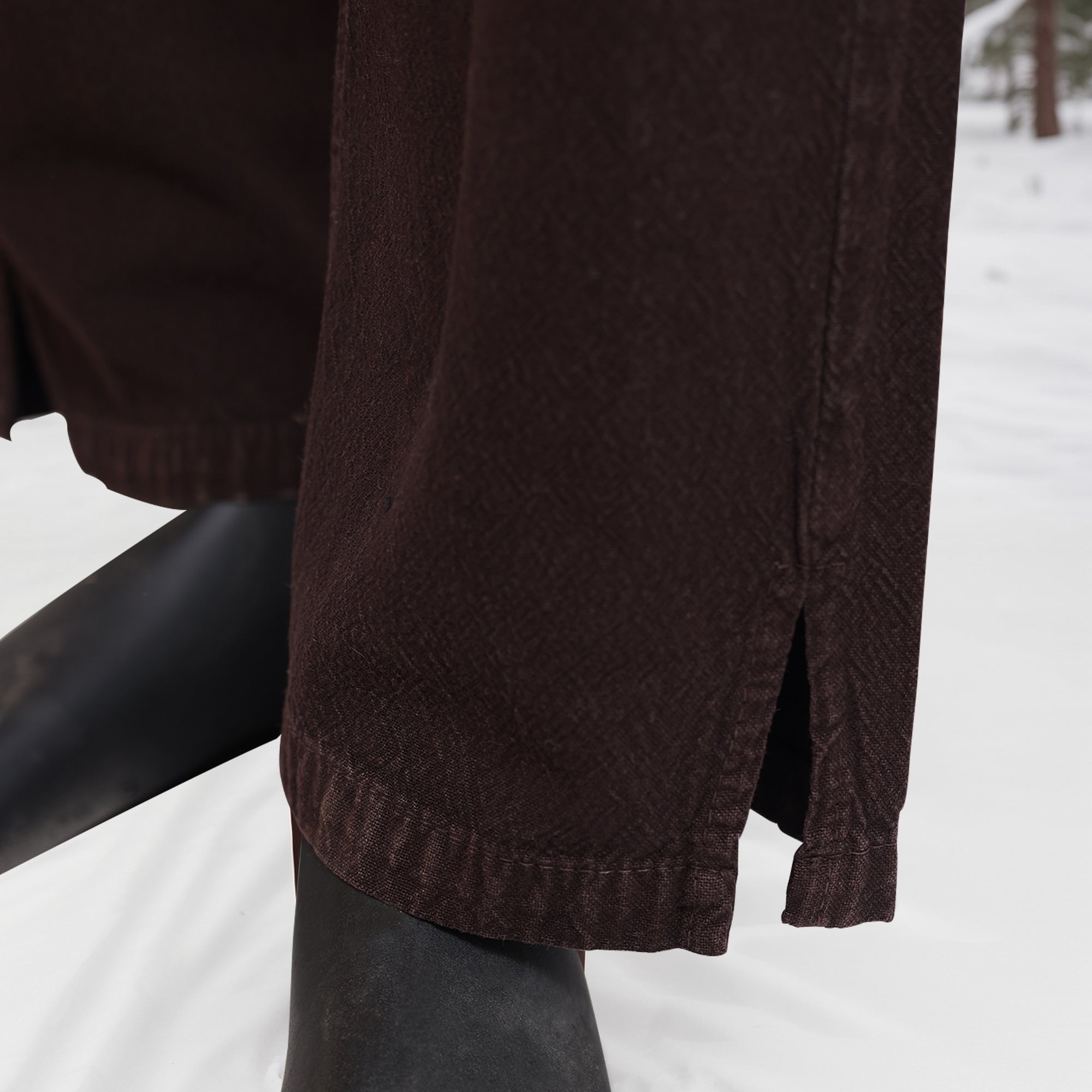 Close-up of lower legs wearing Warrior Pants- Men's, featuring a small side slit at the hem, paired with black boots and standing on snow.