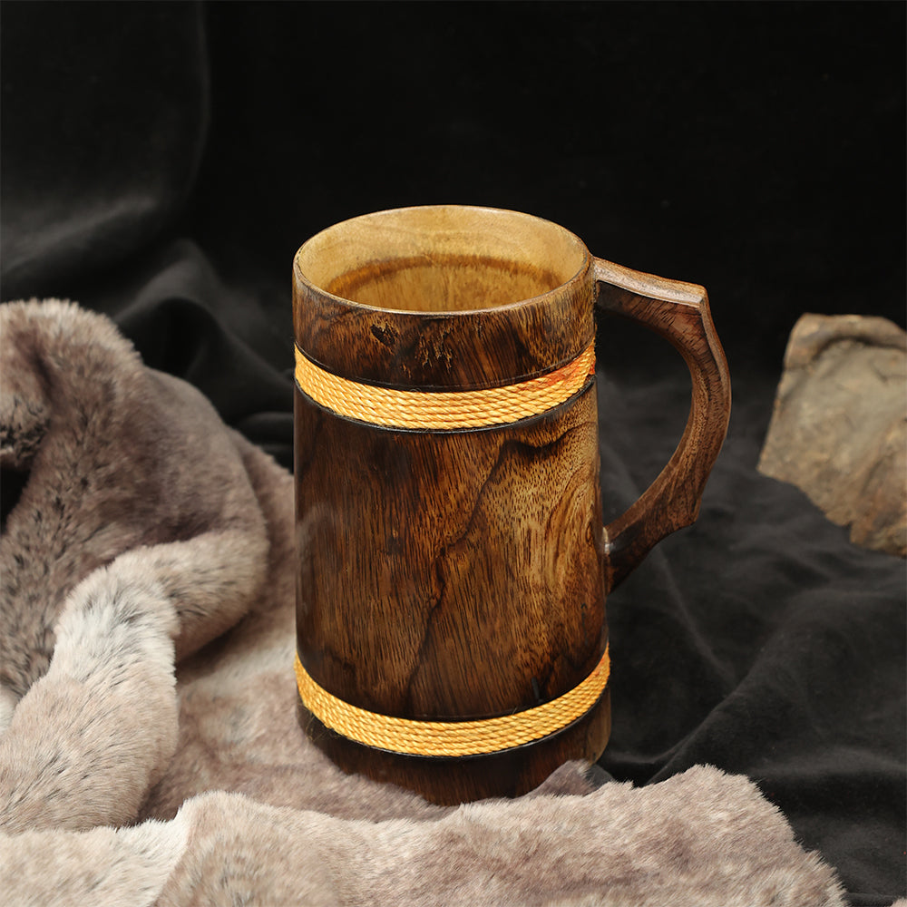 The Wooden Beer Mug with Antique Golden Thread, featuring a handle and two golden bands, rests on a soft, fur-like surface against a dark background.