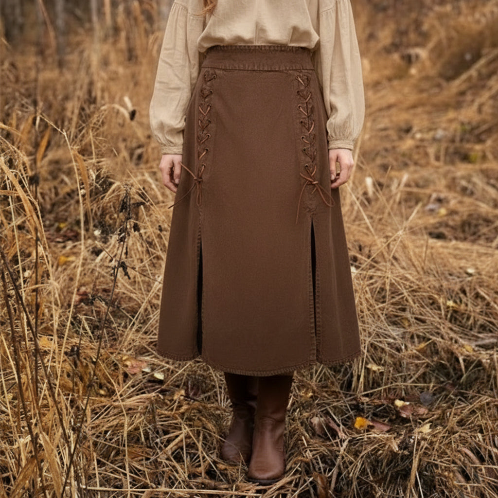 A person stands in dry grass, wearing brown boots and the Medieval Skirt- Ladies with lace-up sides—a perfect choice for a Renaissance fair costume. Only the lower body is visible.