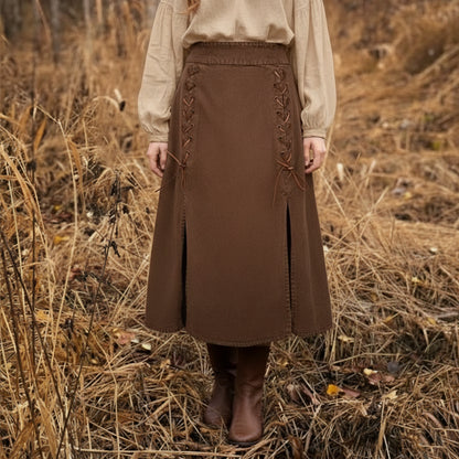A person stands in dry grass, wearing brown boots and the Medieval Skirt- Ladies with lace-up sides—a perfect choice for a Renaissance fair costume. Only the lower body is visible.