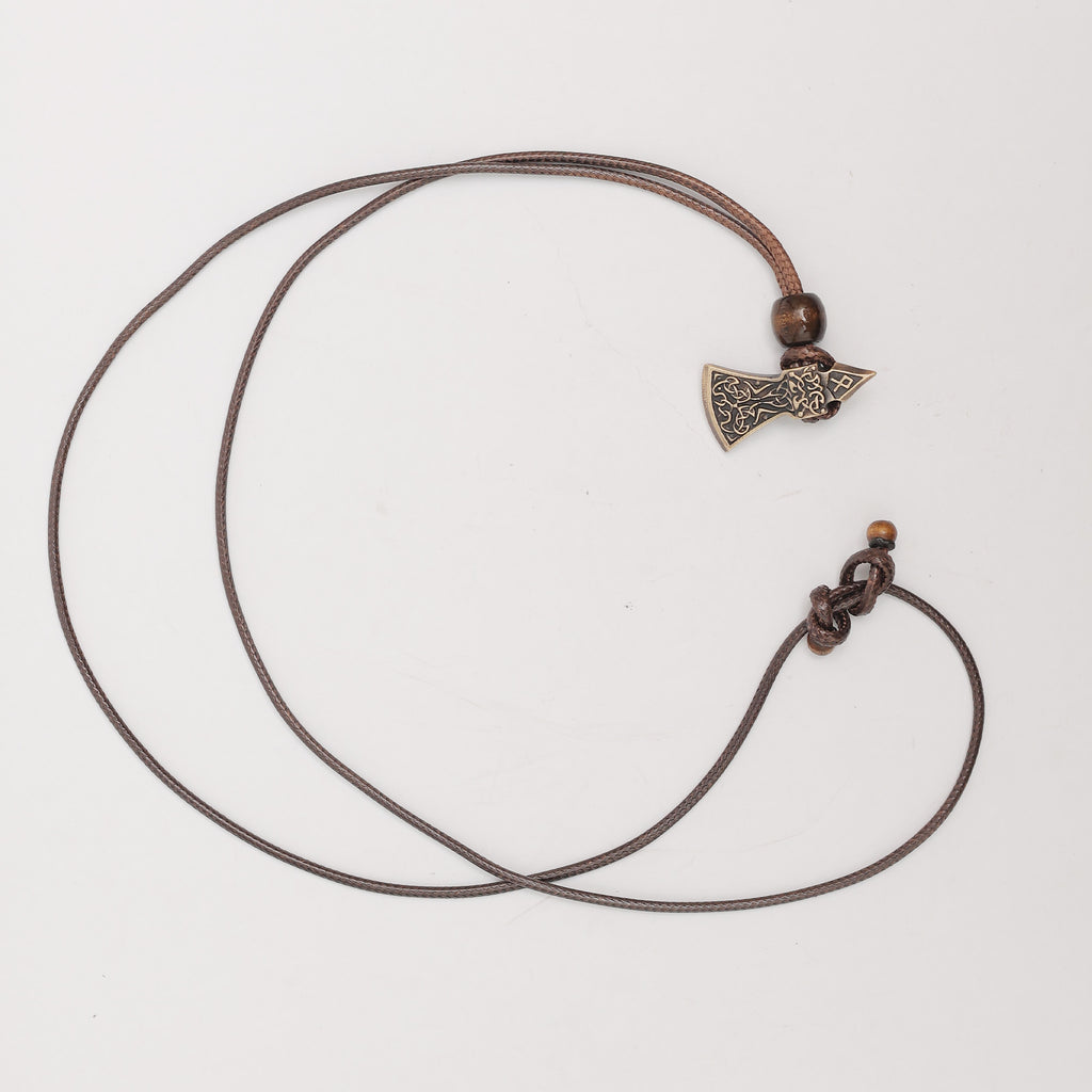 The Viking Axe Brass Pendant features a small, intricately designed axe on a brown cord with wooden bead accents, displayed against a plain white background.