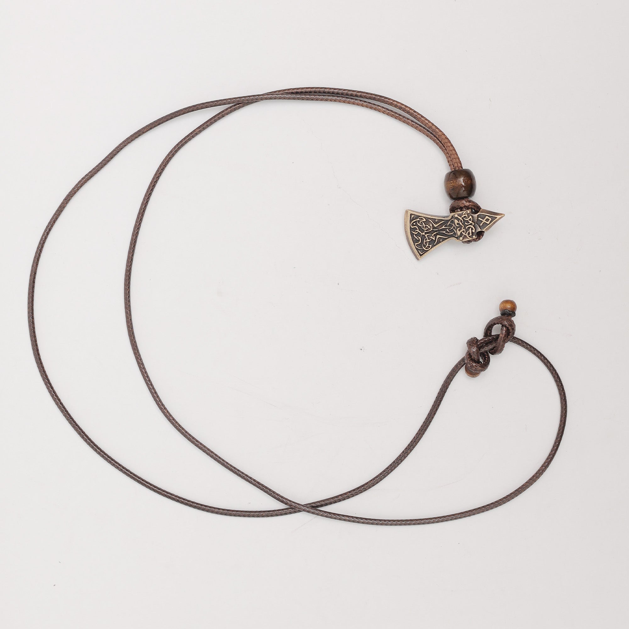 The Viking Axe Brass Pendant features a small, intricately designed axe on a brown cord with wooden bead accents, displayed against a plain white background.