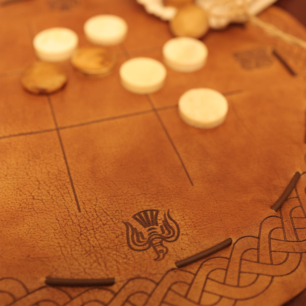 A close-up of the Viking Leather Tic Tac Toe Game, featuring white and brown round pieces on a leather board with Celtic knots and a thistle emblem for a beautifully textured, handcrafted Viking look.