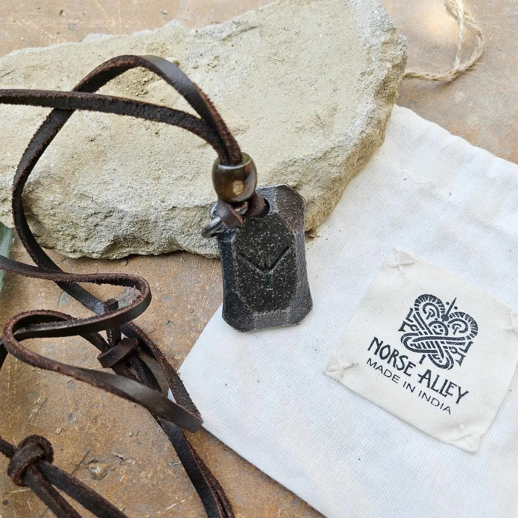 A Viking Rune Pendant Algiz on a leather cord sits next to a rough stone and a white Norse Alley pouch, making it ideal Norse mythology jewelry or a protection pendant for fans of Viking-inspired design.
