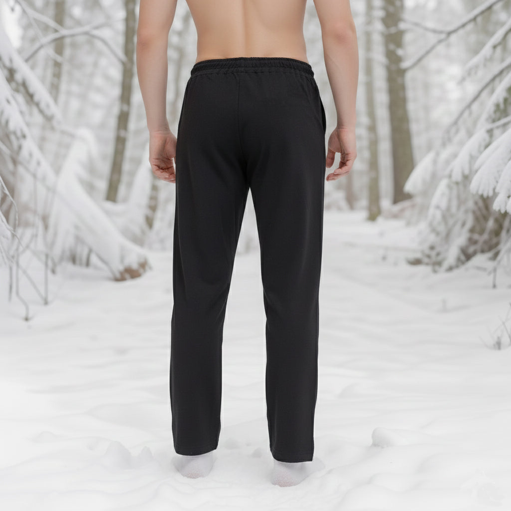 A barefoot man stands shirtless in the snow, wearing Warrior Pants-Men’s among snow-laden trees, evoking Norse reenactment in a wintry forest.