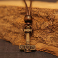 The Norse Alley Thor’s Hammer Pendant features intricate Norse designs on bronze and hangs from a brown cord, making it a bold piece of mythology jewelry.