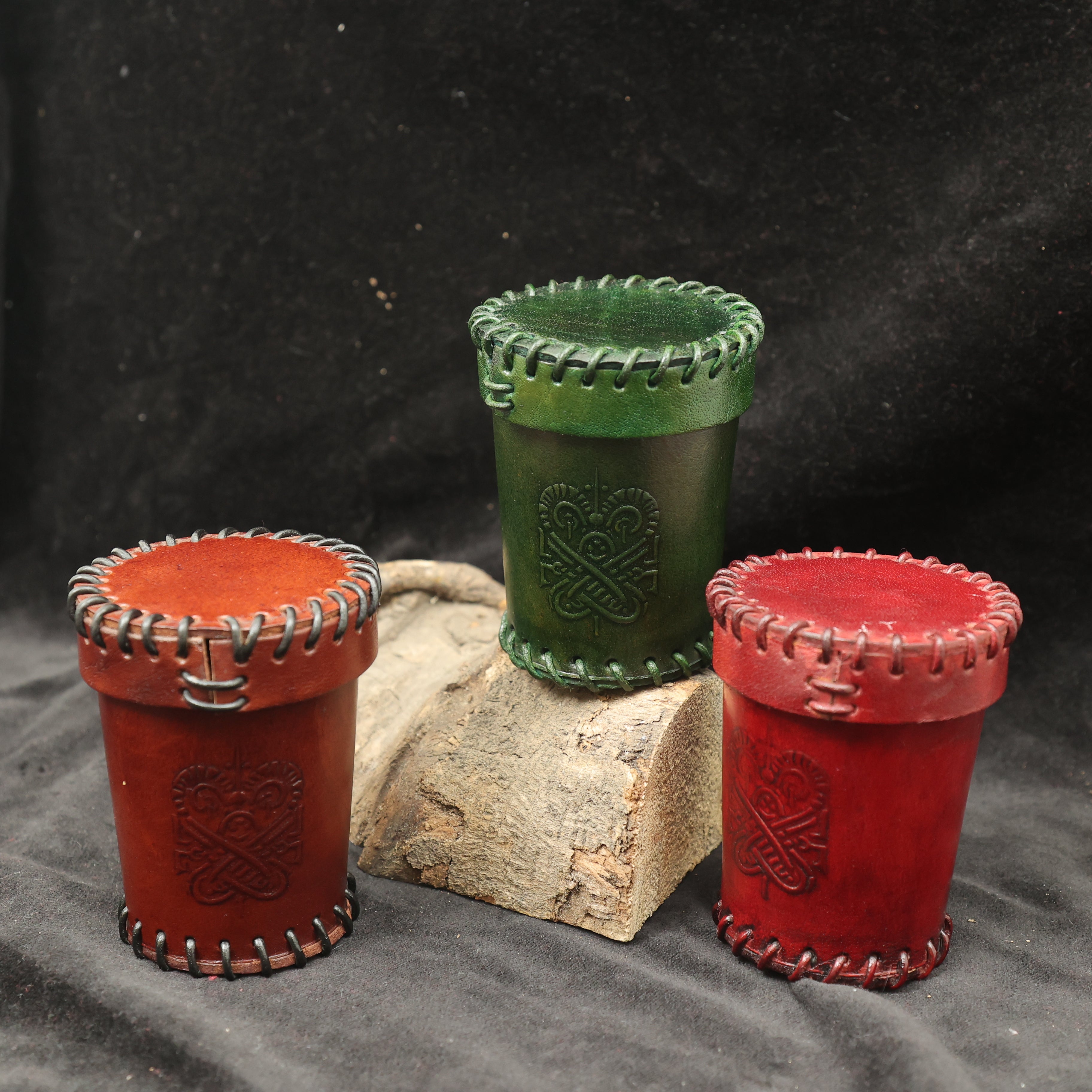 The Handcrafted Dark Red Leather Dice Cup features decorative stitching and embossed designs, making it a perfect tabletop RPG accessory or unique handmade dice cup, styled on wood with a black fabric background.