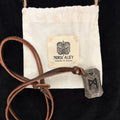 The Viking Rune Pendant Mannaz, a brown leather necklace featuring the powerful Mannaz symbol from Norse mythology, rests on a white Norse Alley pouch labeled "Made in India" with a black Viking-inspired logo.