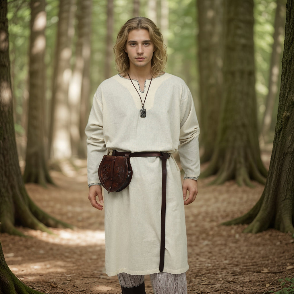 A young person in the Viking Thorndale Tunic–Men’s, with long blond hair and a belt and pouch, stands on a sunlit forest path among tall trees, embodying the feel of historical reenactment.