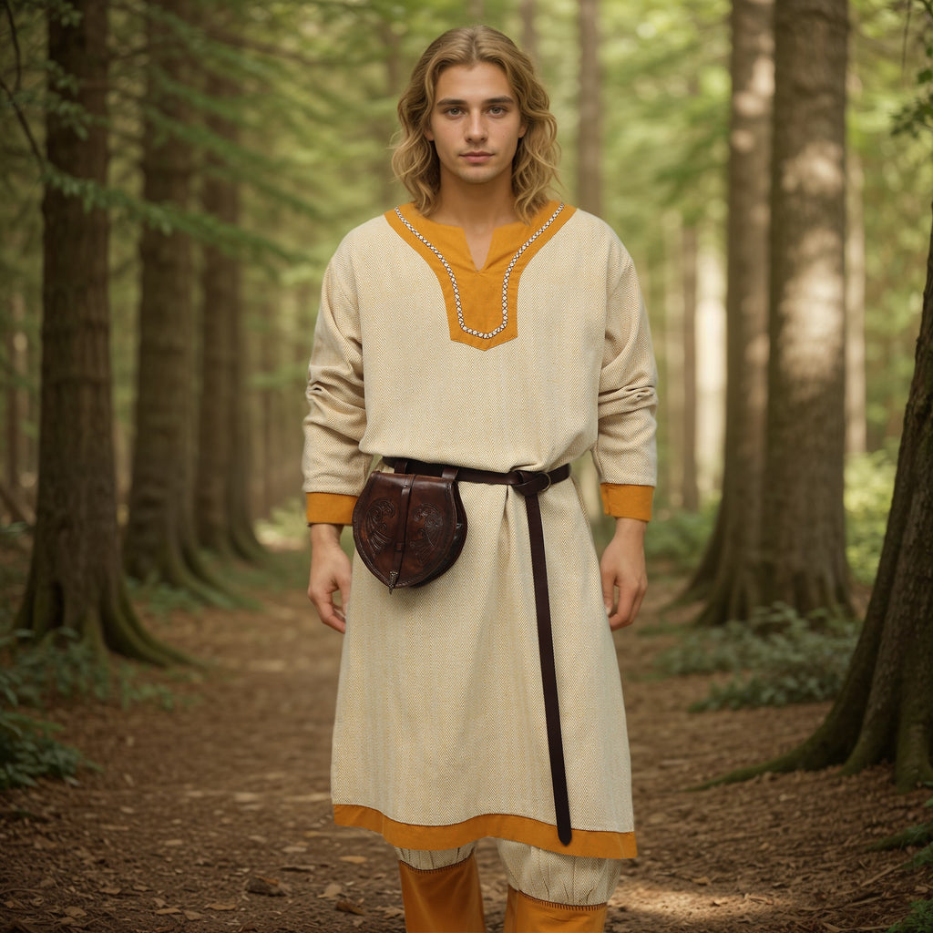 A young person with long blonde hair stands on a forest path, wearing the Nordic Runeweave Viking Tunic- Men's in beige with orange trim, paired with a brown belt and pouch, surrounded by tall trees and lush greenery.