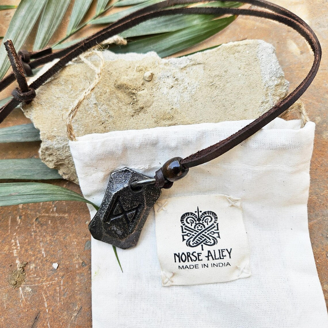 The Viking Rune Pendant Dagaz hangs on an adjustable leather cord atop a white Norse Alley bag labeled Made in India, with a stone and palm leaves in the background.