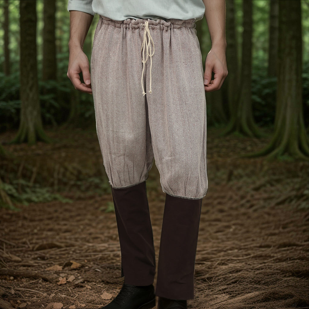 A person stands in a forest wearing Nordic Nomad Viking Pants with a drawstring waist and dark brown gaiters over black shoes—ideal for a Nordic reenactment costume. Their upper body is mostly out of frame.