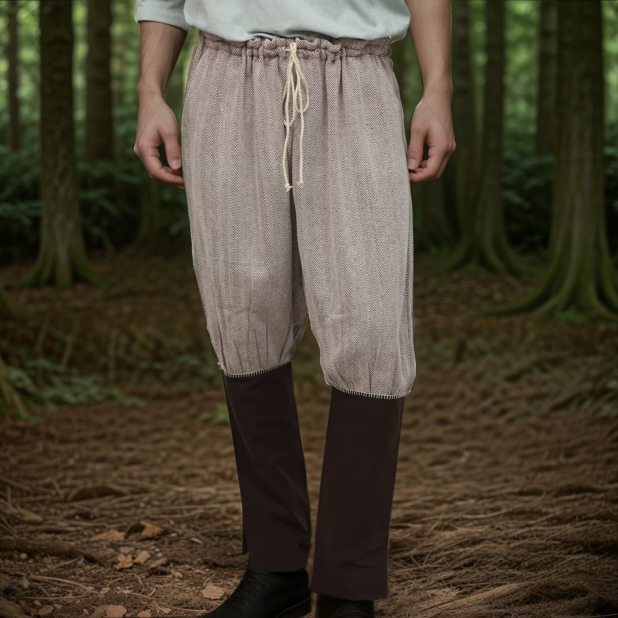 A person stands in a forest wearing Nordic Nomad Viking Pants with a drawstring waist and dark brown gaiters over black shoes—ideal for a Nordic reenactment costume. Their upper body is mostly out of frame.
