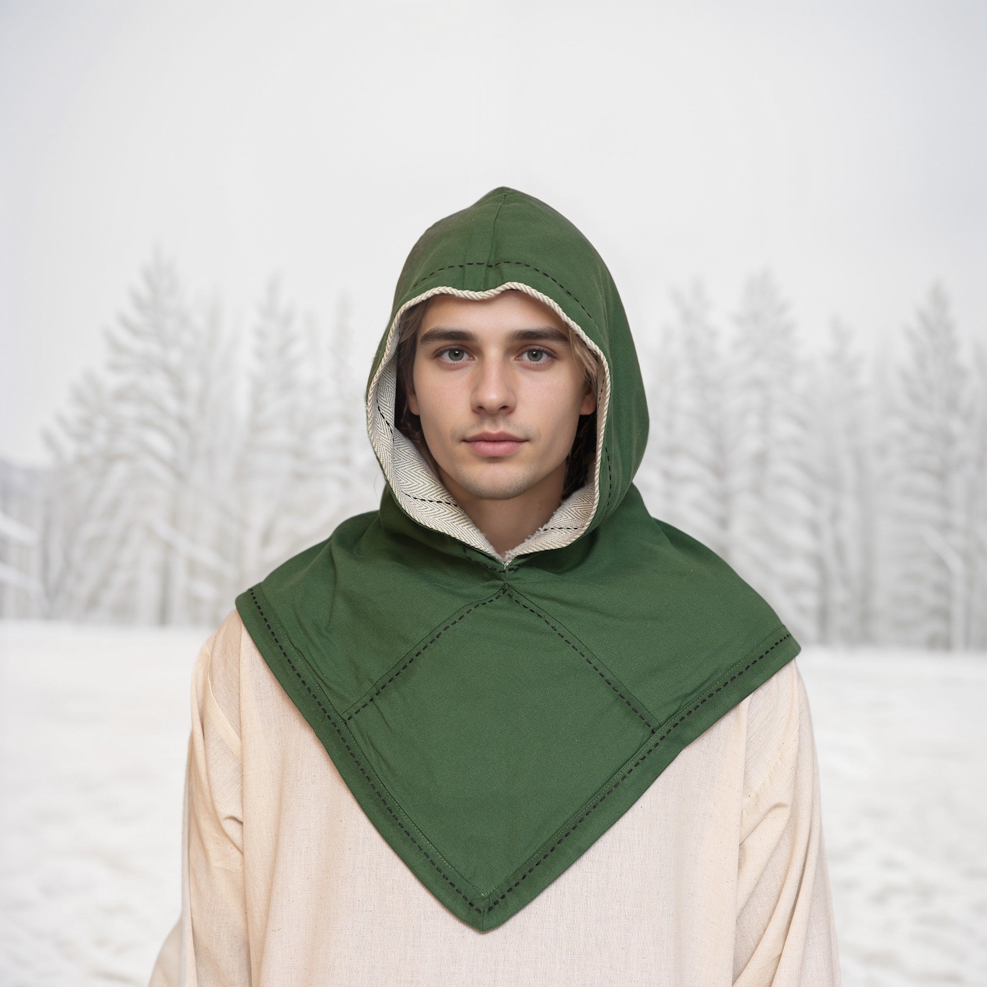 A young person outdoors in a snowy landscape wears a green Reversible Viking Hood, Skjoldehamn, over a light beige garment, evoking the spirit of medieval reenactment amid frosted trees.
