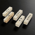 The Viking Bone Dice Set of 5 features rectangular, ivory-toned dice with black dots, arranged on a dark, textured surface. Each piece displays a unique number and orientation, reminiscent of medieval gaming accessories.