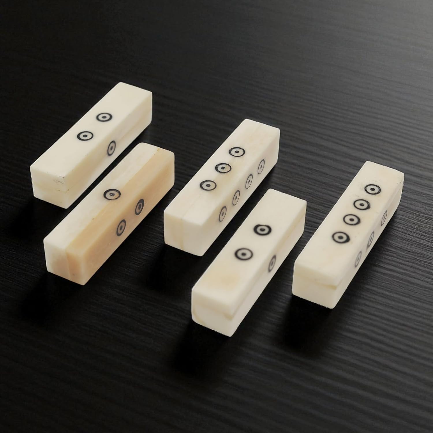 The Viking Bone Dice Set of 5 features rectangular, ivory-toned dice with black dots, arranged on a dark, textured surface. Each piece displays a unique number and orientation, reminiscent of medieval gaming accessories.