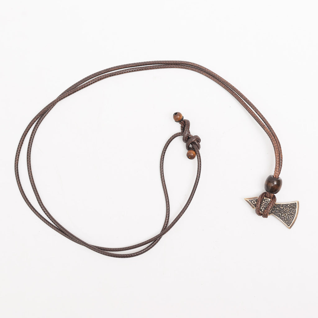 The Viking Axe Brass Pendant is a brown cord necklace with two wooden beads and a detailed, engraved axe pendant, showcased on a white background.