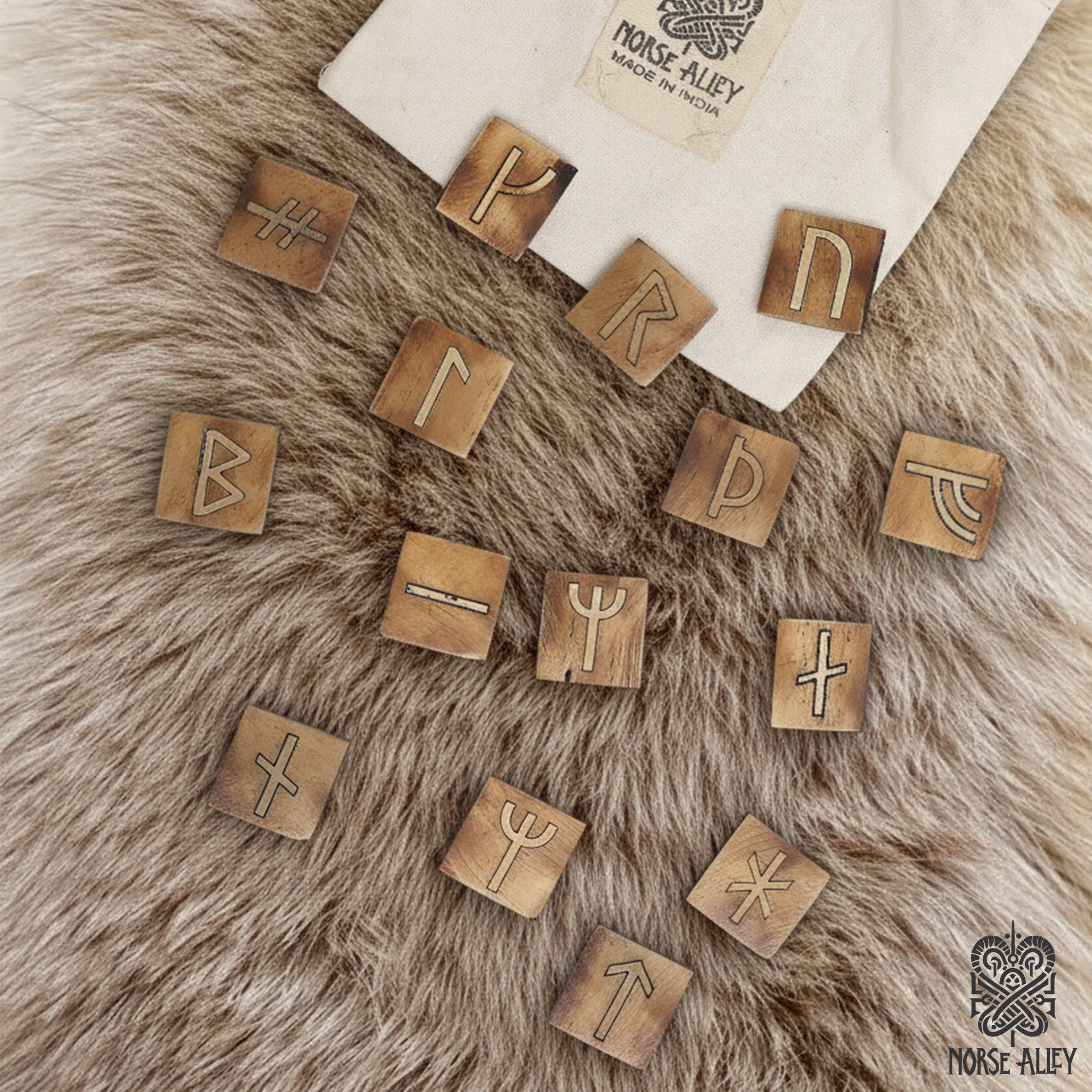 Handcrafted wooden tiles from the Younger Futhark Rune Set – 16 Handcrafted Tiles are laid out on a soft surface. A fabric pouch featuring the Norse Alley logo and “Made in India” is partially visible in the corner.
