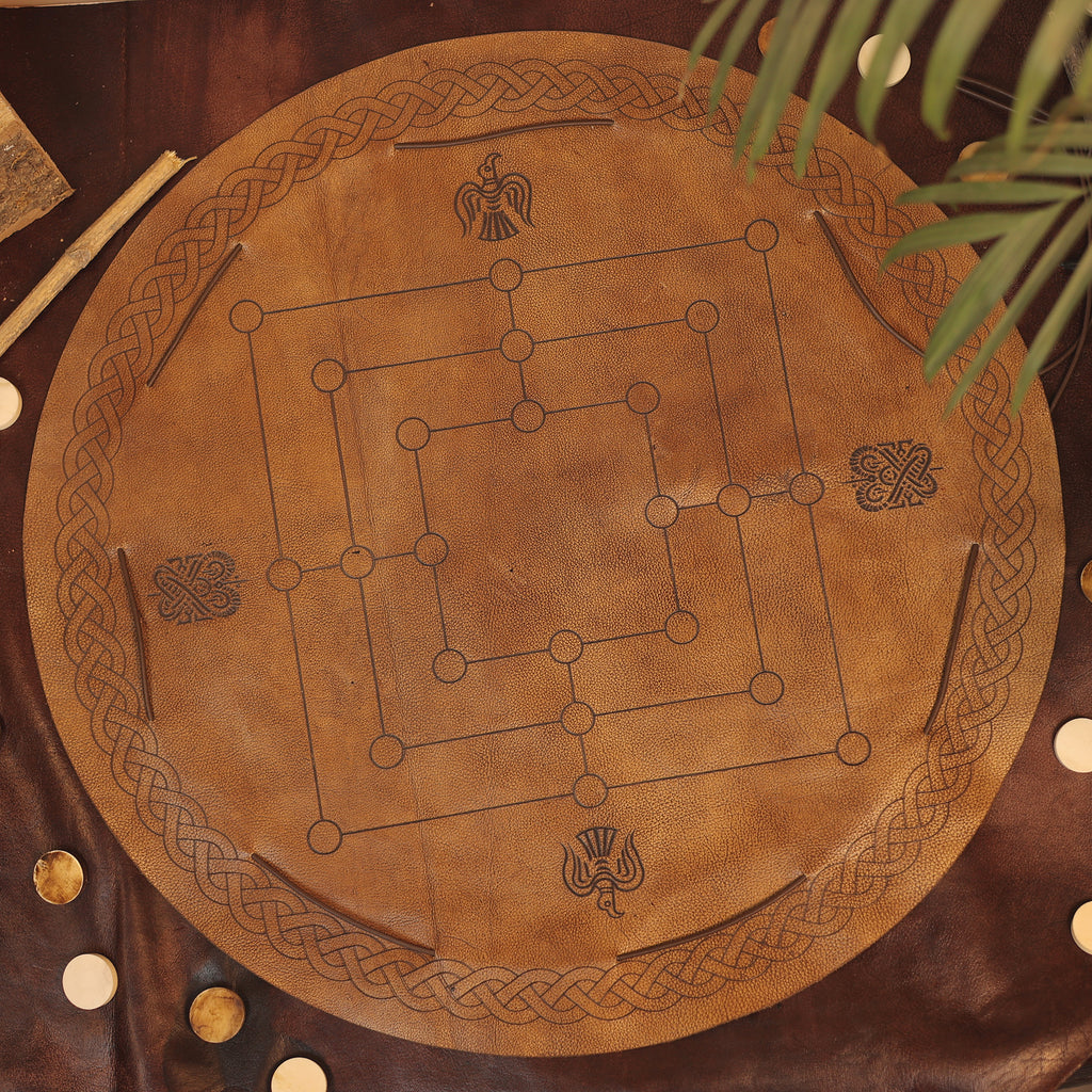 The Nine Men's Morris features a round leather game board with Celtic knot and bird designs, wooden pieces, and a visible plant leaf in the corner—bringing classic two-player strategy gameplay with elegant details.