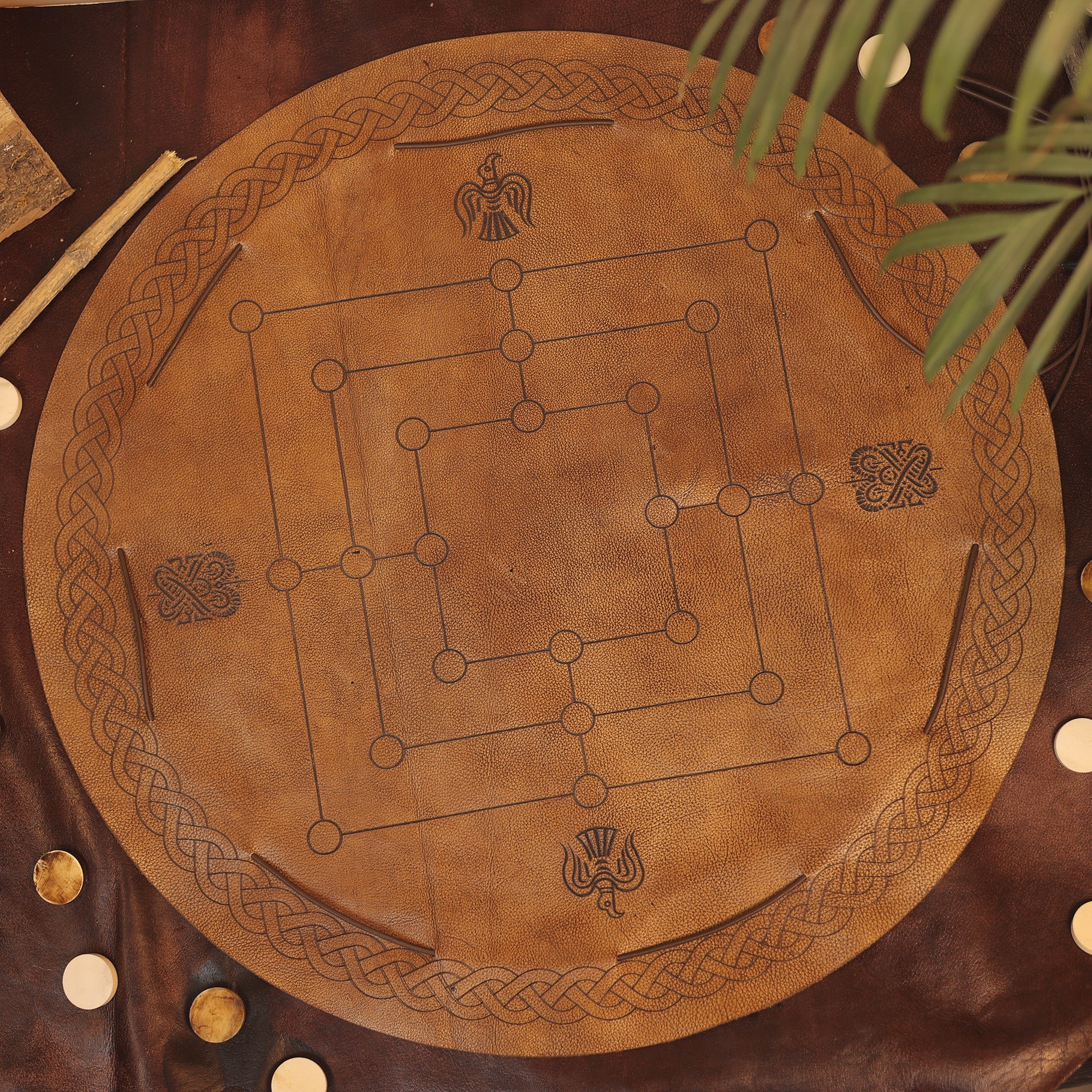The Nine Men's Morris features a round leather game board with Celtic knot and bird designs, wooden pieces, and a visible plant leaf in the corner—bringing classic two-player strategy gameplay with elegant details.