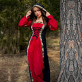A woman in the Dark Majesty Medieval Dress for ladies, featuring red and black fabric with gold trim, stands by a tree in a forest, lifting her hood—a perfect choice for LARP clothing or Renaissance fair costumes.