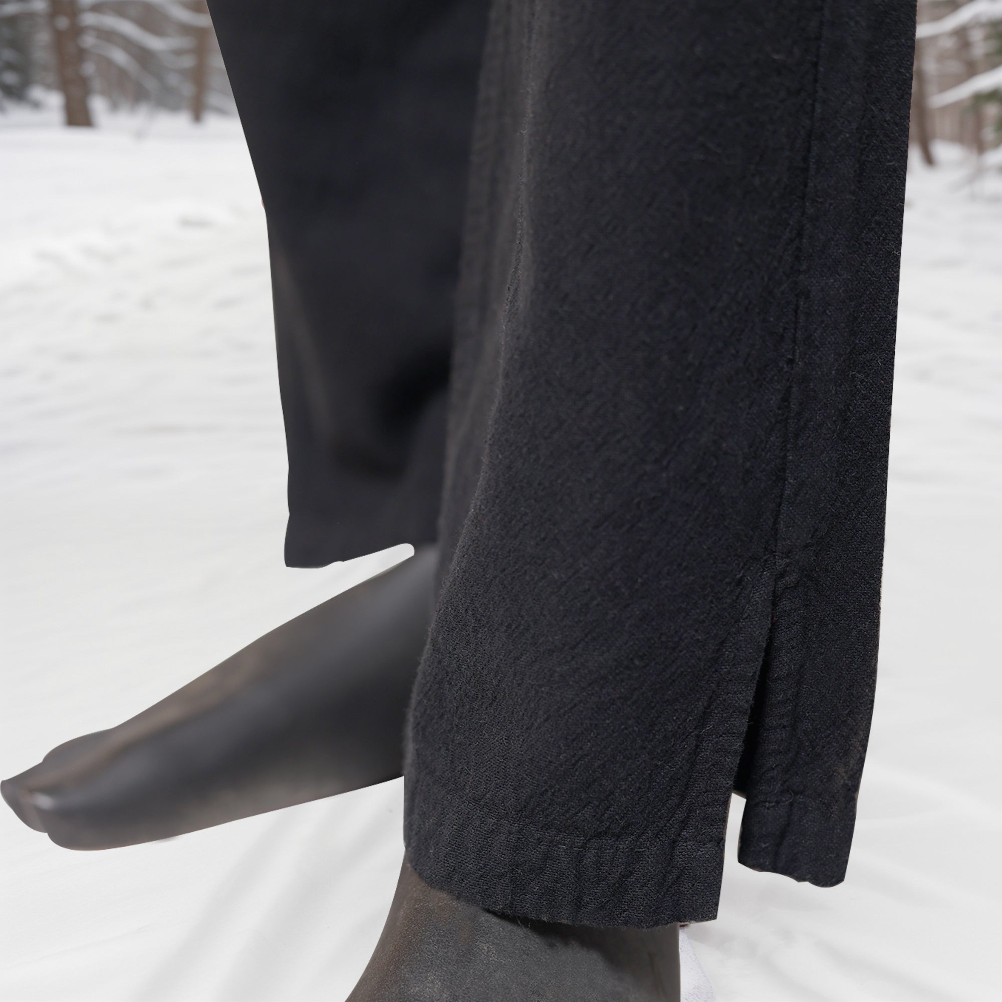Close-up of a person standing barefoot on snow, wearing Warrior Pants- Men's in black. The setting features snow-covered ground and trees, highlighting the pants' Viking-inspired style suited for cold outdoor conditions.