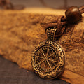 A close-up of the Nomad's Compass Pendant, featuring intricate engravings and a compass motif, hanging from a braided brown leather cord against rustic wood—a striking piece of Norse-inspired travel jewelry.