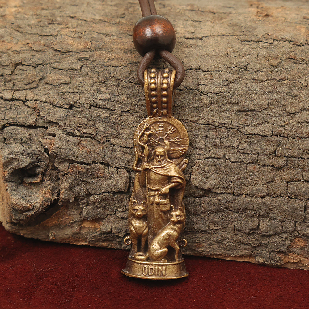 The Odin Pendant – The Allfather is a bronze brass pendant showing Odin with a spear, two wolves, and Norse symbols above. It hangs from a leather cord with a wooden bead, presented on rough tree bark.